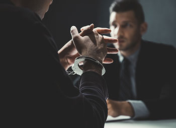 Two men in suits sitting at a table, one with handcuffs - Coren Law Group P.C.