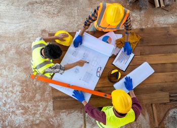 Three construction workers in hard hats and safety vests laboring at a construction site. - Coren Law Group P.C.